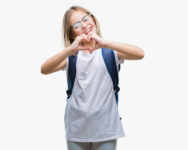 年轻，美丽，聪明的学生女孩，穿着背包，在孤立的背景上微笑，在爱中，用手展示心脏的象征和形状。 浪漫的概念。