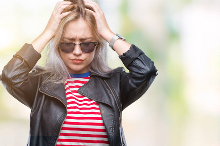 年轻的金发女人穿着时尚夹克和太阳镜，在孤立的背景下，因为疼痛和偏头痛而感到头痛绝望和压力。 手放在头上。