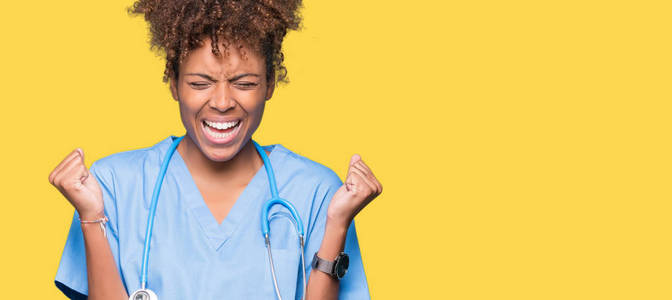 年轻的非裔美国医生女人在孤立的背景下庆祝疯狂和疯狂的成功，举起手臂和闭上眼睛尖叫兴奋。 赢家概念