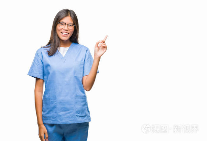 年轻的亚洲医生女人在孤立的背景上，脸上带着大大的微笑，用手和手指指向一边，看着相机。