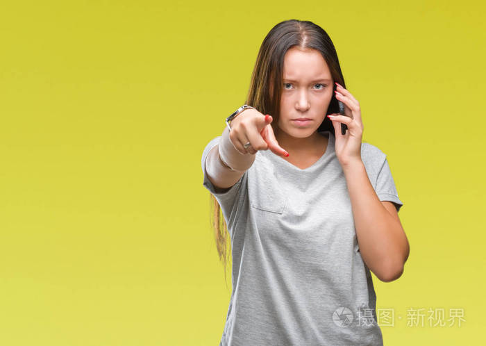 年轻美丽的高加索女人在智能手机上交谈，在孤立的背景下，手指指向相机，向你手势正面和自信的手势。