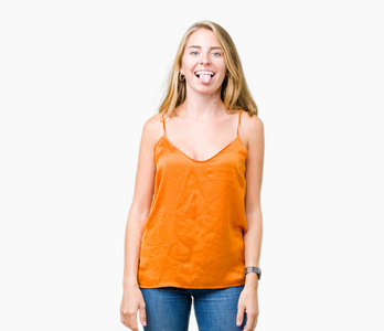 美丽的年轻女子穿着橙色衬衫，在孤立的背景上伸出舌头，以有趣的表情高兴。 情感概念。