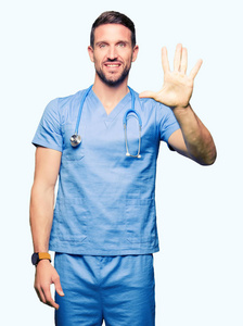 英俊的医生男子穿着医疗制服，在孤立的背景上显示和举着手指第五，同时微笑自信和快乐。