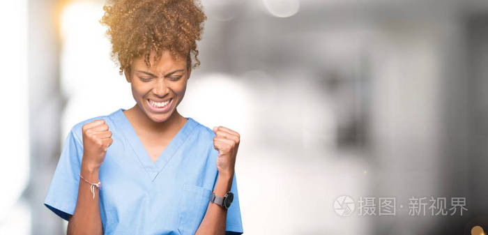年轻的非裔美国医生女人在孤立的背景下，非常高兴和兴奋地做胜利者的手势，举起手臂，微笑和尖叫，争取成功。 庆祝概念。