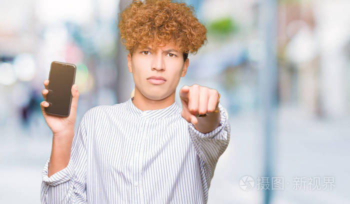 年轻的帅哥展示智能手机屏幕,手指指向相机和你的手势,正面的积极和