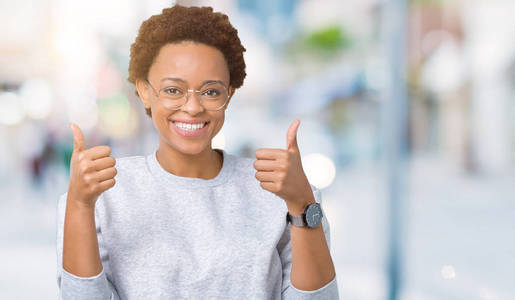 年轻美丽的非洲裔美国妇女戴着眼镜，在孤立的背景上，成功标志，用手竖起大拇指，微笑和快乐地做积极的手势。 用欢快的表情看着相机，胜