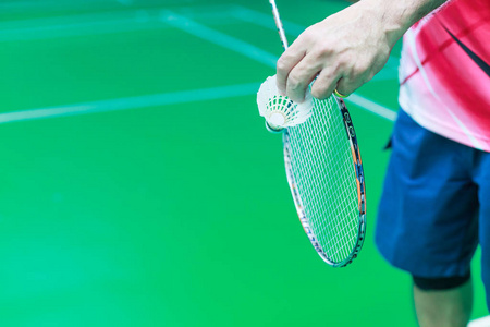 班车公鸡男羽毛球单人手拿着白色的穿梭公鸡和球拍,准备在绿色球场上