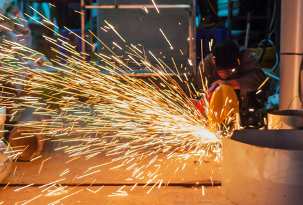 在施工现场,在工厂对钢结构进行电轮磨削的焊接工人照片