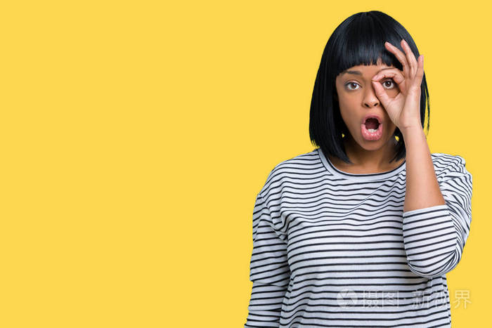 年轻非洲裔美国妇女穿着条纹毛衣,在孤立的背景上做着ok手势,惊讶的脸