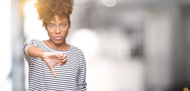 美丽的年轻非洲裔美国妇女戴着眼镜，在孤立的背景上看起来不高兴和愤怒，表现出拒绝和消极的拇指向下的手势。不好的表情。