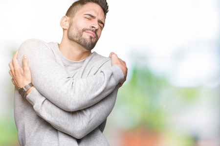 年轻的帅哥穿着运动衫在孤立的背景下拥抱自己,快乐而积极,微笑自信.