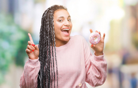 年轻的非洲裔美国女孩吃粉红色甜甜圈，在孤立的背景惊讶的想法或问题，手指与快乐的脸，第一