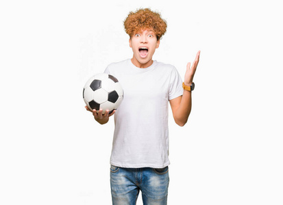 年轻的帅哥捧着足球，非常高兴和兴奋，胜利者的表情庆祝胜利，微笑着尖叫，举起双手