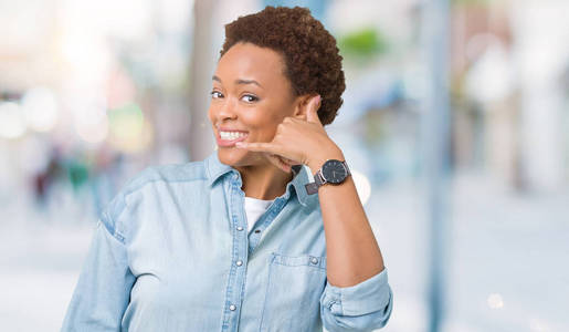 年轻美丽的非洲裔美国妇女在孤立的背景下微笑着做电话手势，用手和手指，就像在电话上交谈。 交流概念。