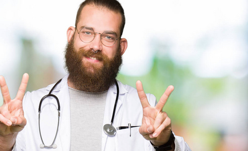 年轻的金发医生，胡须男，穿着医疗外套，微笑着看着镜头，手指在做胜利标志。 二号。
