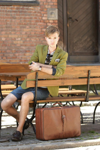 年轻帅哥提着手提箱坐在长凳上等着