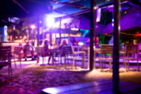 在夜晚，热带海滩俱乐部酒吧与沙滩人和紫色灯光失去了焦点