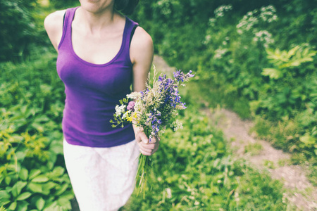 那个女孩拿着一束野花。 女性手中的紫罗兰花。 一个女人正在草地上摘花。