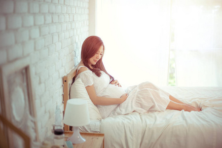 迷人的亚洲孕妇躺在床上,抱着她的肚子照片