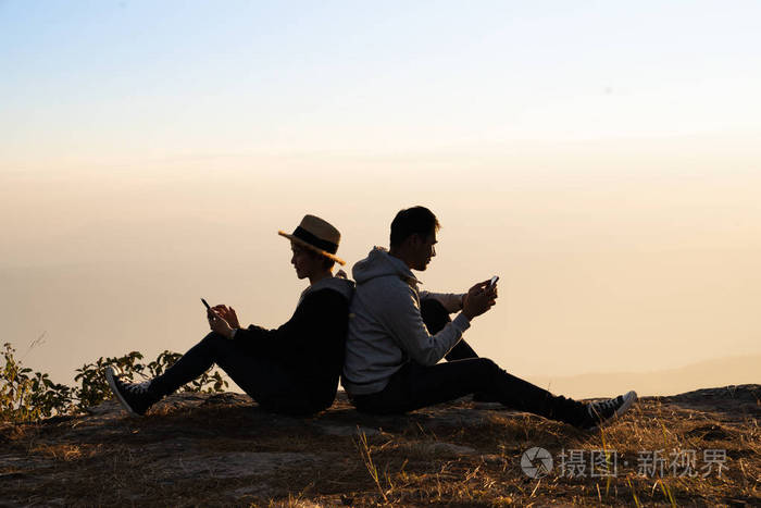 一对夫妇背靠背坐在自然环境中使用智能手机的剪影