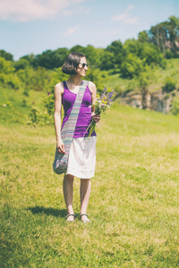 那个女孩拿着一束野花。 一个女人在炎热的夏天穿过草地。