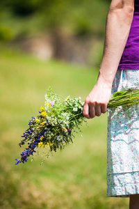 那个女孩拿着一束野花。 雌性手拿着草甸花。 在田野上走。