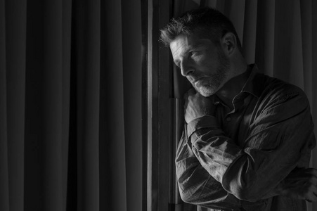 夜晚窗边年轻帅气悲凉沮丧的男人绝望地承受着抑郁的折磨感到心碎的