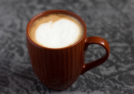 灰色背景棕色杯子里的热卡布奇诺咖啡