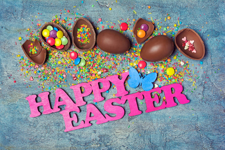 在蓝色的混凝土背景上，可以看到粉红色的复活节和巧克力传统鸡蛋，上面有鲜艳的悬垂和糖洒或纸屑