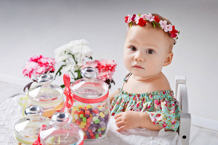 小快乐的蹒跚学步的女孩庆祝一岁生日。 可爱的女婴坐在桌旁，用糖果棒