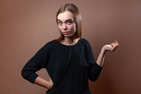 美丽的年轻女子神秘地看着一件米色背景的黑色毛衣的框架