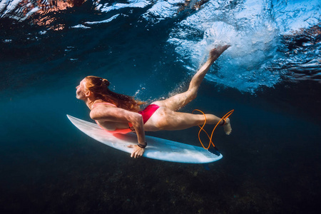 迷人的冲浪女子在波浪下潜水。