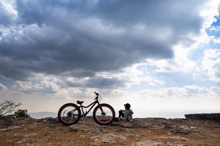 一个人坐在岩石山上的自行车旁，眺望美丽的自然景色和美丽的蓝天