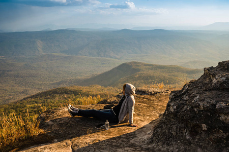 一个女人坐在岩石山上，眺望美丽的自然景色和美丽的蓝天