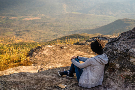 一个女人坐在岩石山上，眺望美丽的自然景色和美丽的蓝天