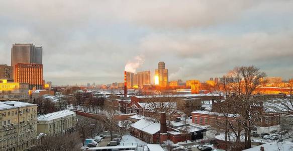 在莫斯科的黎明，房子和美丽的城市日出反射在高耸的窗户和摩天大楼的窗户上，在一个寒冷的冬天的早晨，明亮的天空云和工厂管道中的烟雾