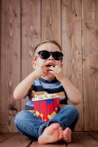 小可爱的孩子，小男孩，2，3岁的3D电影院眼镜，拿着水桶吃爆米花，在木制背景下吃快餐。 儿童童年生活方式的概念。 复制空间。