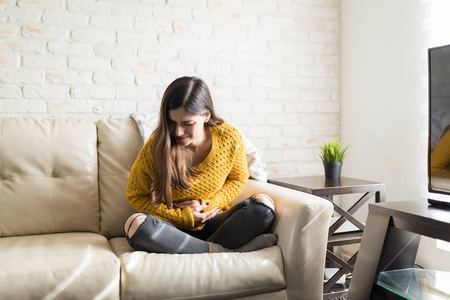 黑发女人坐在沙发上肚子疼照片