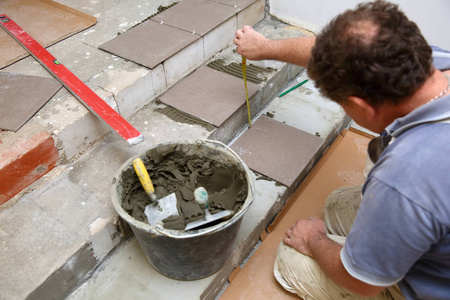建筑工人用铲子测量地板，以便很好地安排楼梯上瓷砖的铺设。