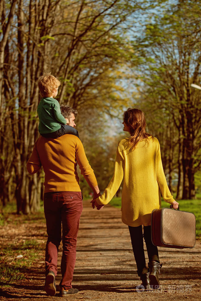 沿着公园路的家庭旅行父亲给儿子背驮而母亲背着旅行