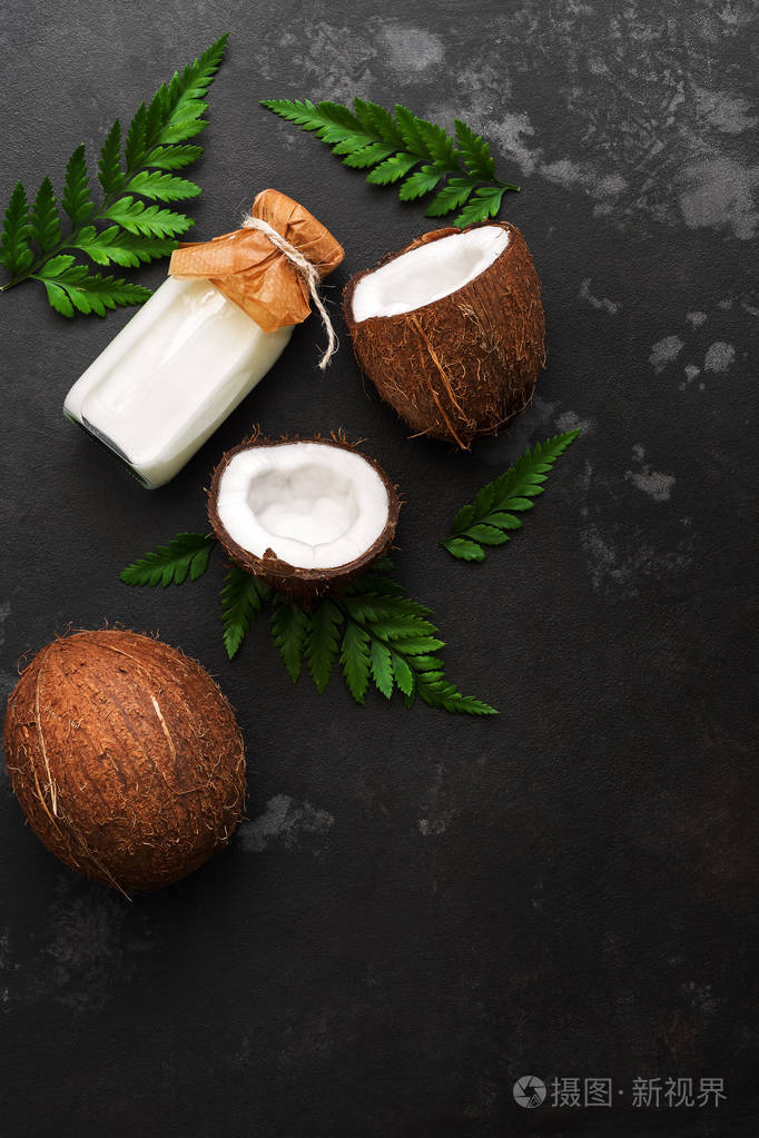 椰子和牛奶在一个瓶子上的深色石头背景装饰着蕨类植物的叶子.