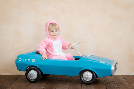 穿复活节兔子的有趣孩子。 孩子在家骑玩具车。 春假概念