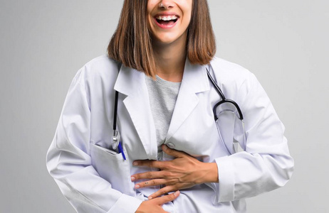 女医生用听诊器微笑，双手放在灰色背景的胸部