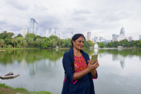 在公园使用手机的成熟的印度妇女的肖像