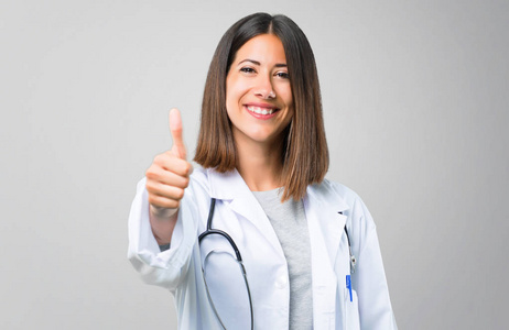 有听诊器的女医生竖起大拇指，微笑着，因为灰色背景下发生了一些好事