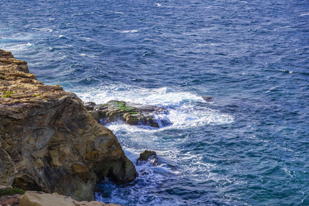 地中海岩石海岸附近有泡沫的如画的海浪，被黎明的太阳照亮