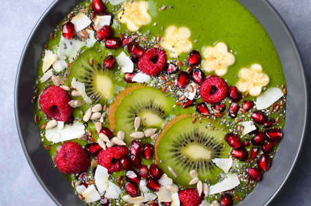 健康的早餐排毒绿色冰沙，香蕉和菠菜，上面有种子和浆果，在碗，纯素膳食顶部观看