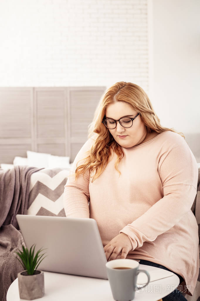 忙碌的长发妇女在呆在家里的时候用她的笔记本电脑工作