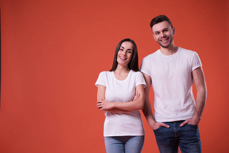 漂亮的年轻夫妇穿着白色空白T恤在橙色背景上摆姿势。 家庭广告