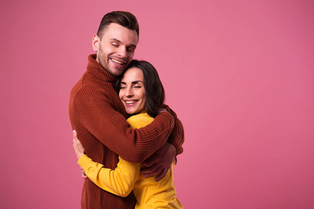 年轻快乐的情侣穿着毛衣，在粉红色的背景下拥抱